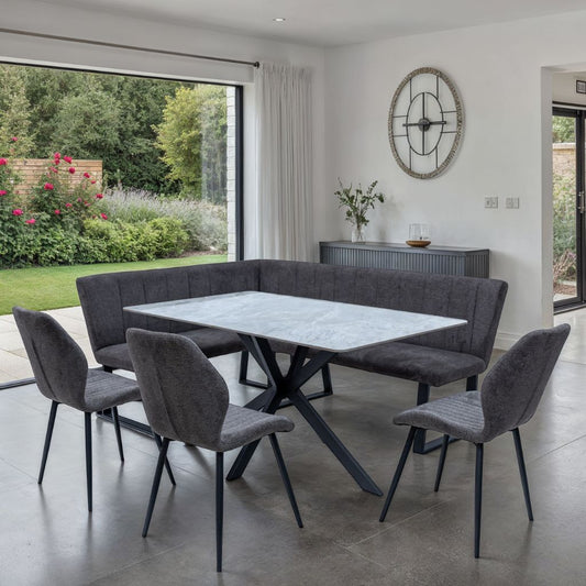 Modern dining area with gray upholstered chairs and bench around a marble table, large window showing garden view.