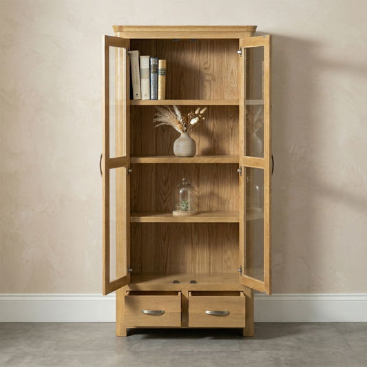 A tall light oak wood display cabinet with two glass doors, open to show interior shelves, two lower drawers.