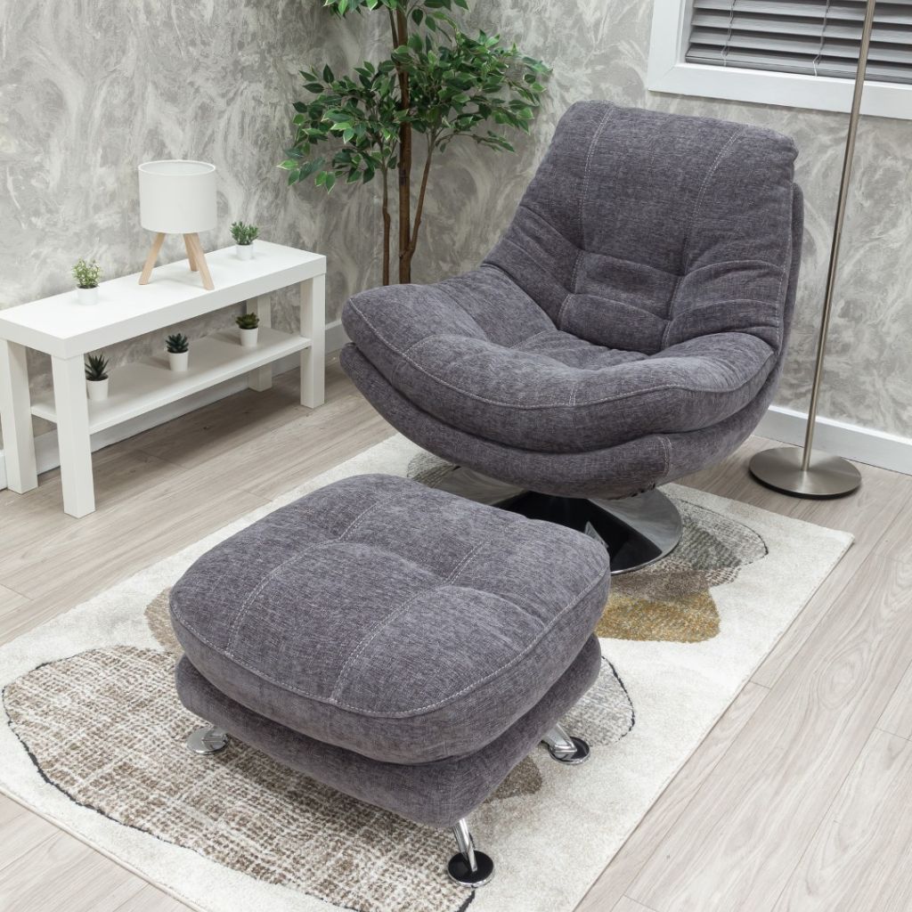 Gray upholstered chair with ottoman in a room setting with a white table and plant.