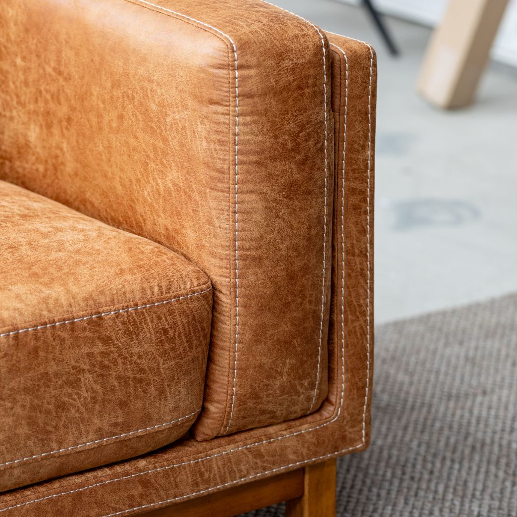 Close-up of a warm tan leather sofa armrest with visible contrast stitching and a wooden leg.