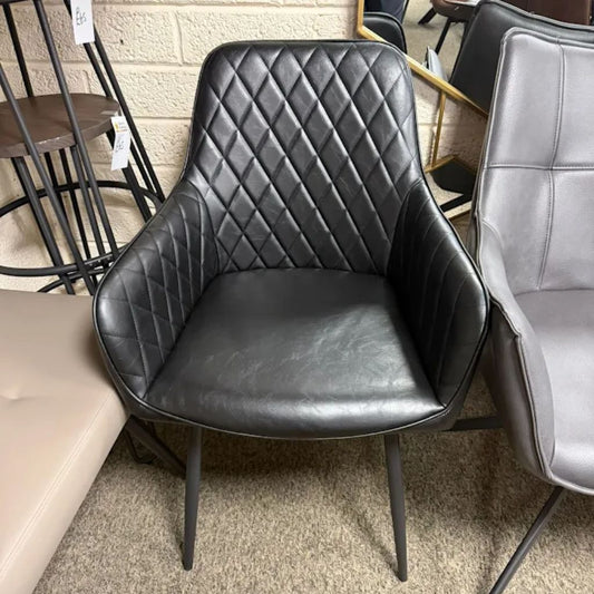Black quilted chair in a store setting with other furniture items.