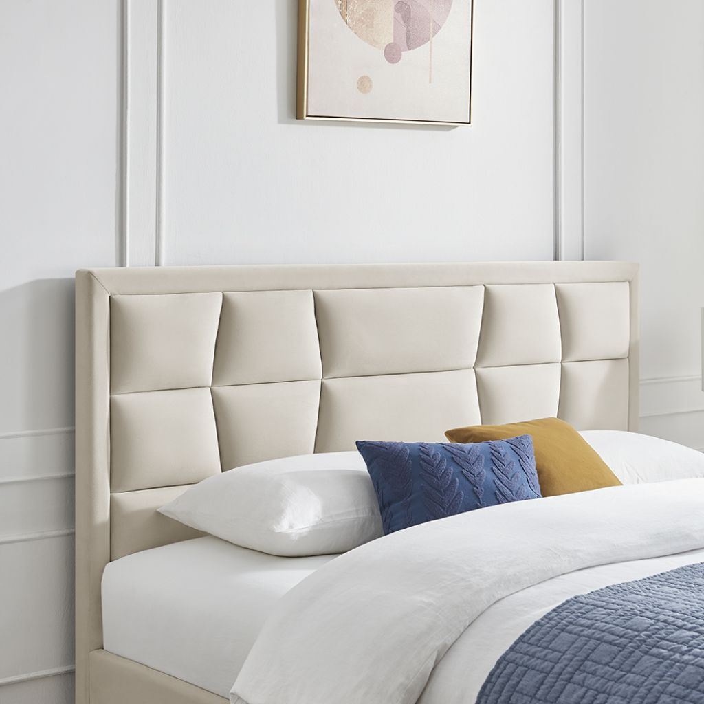 Beige upholstered headboard with pillows on a bed against a white wall.