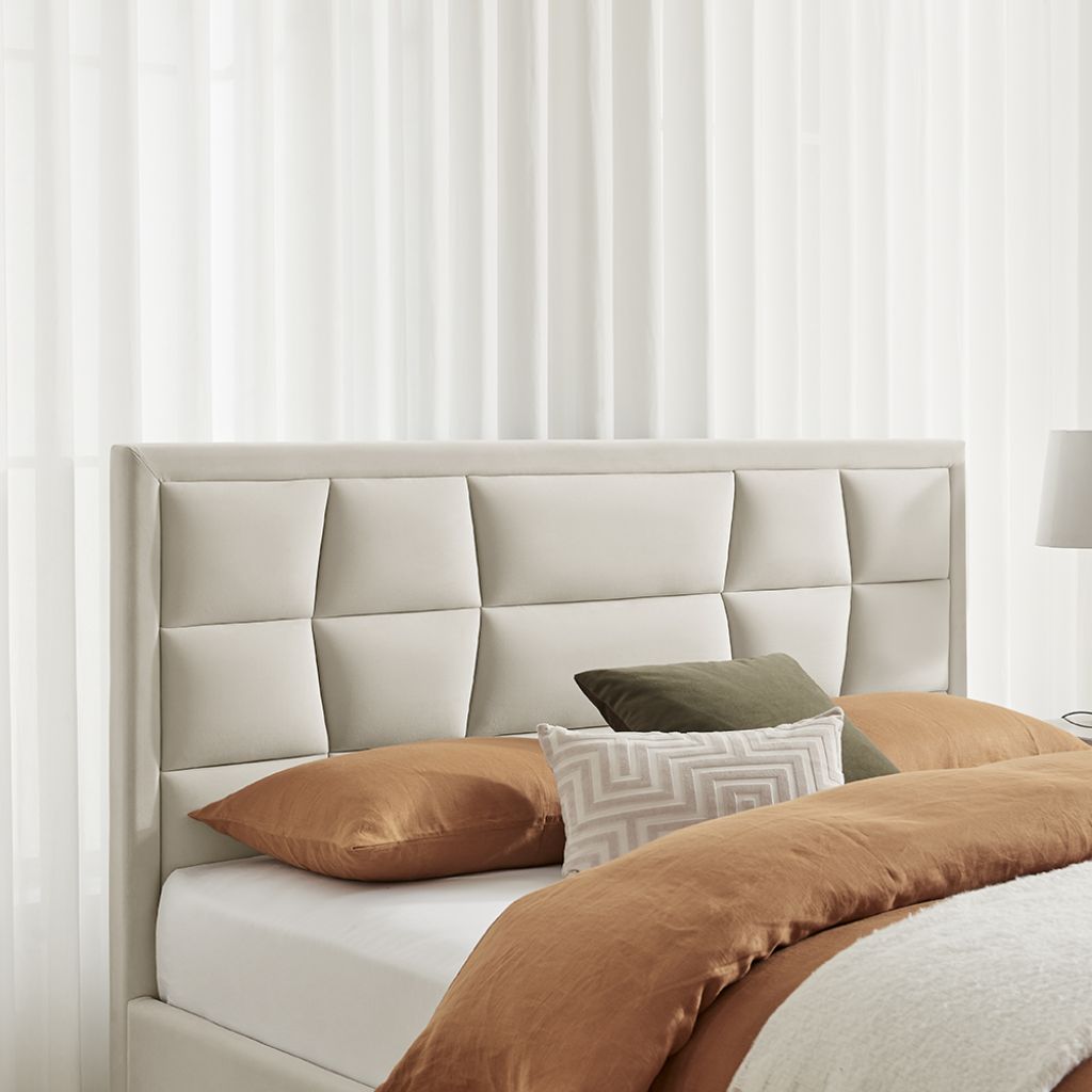 Bed with beige headboard and brown bedding against white curtains