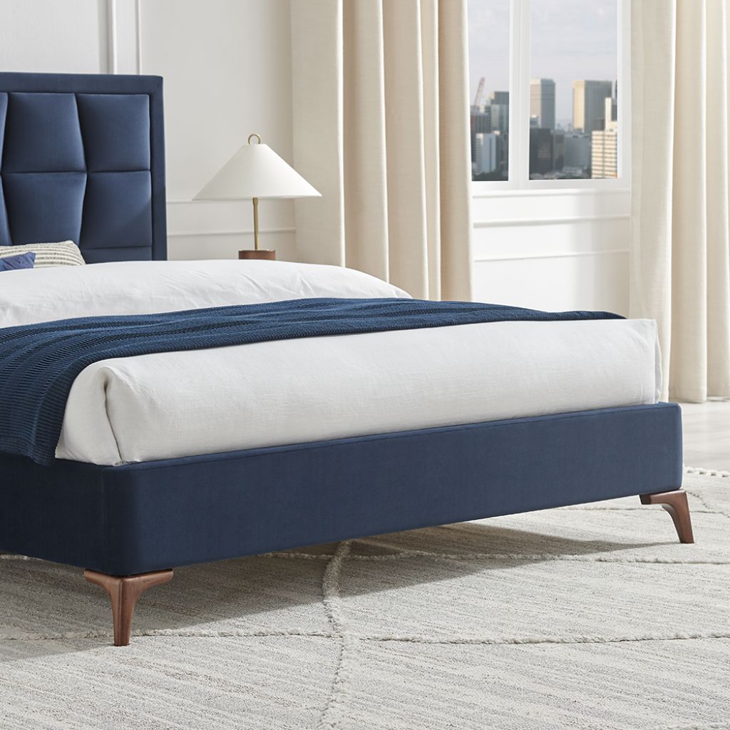 Navy bed frame with white bedding in a room with large windows and curtains.