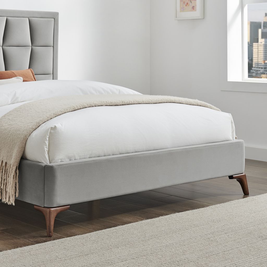 Gray upholstered bed with white bedding and a beige blanket in a bedroom setting.