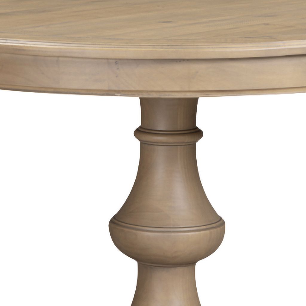Close-up of a round wooden table with a turned pedestal leg in a rustic pine wood finish.