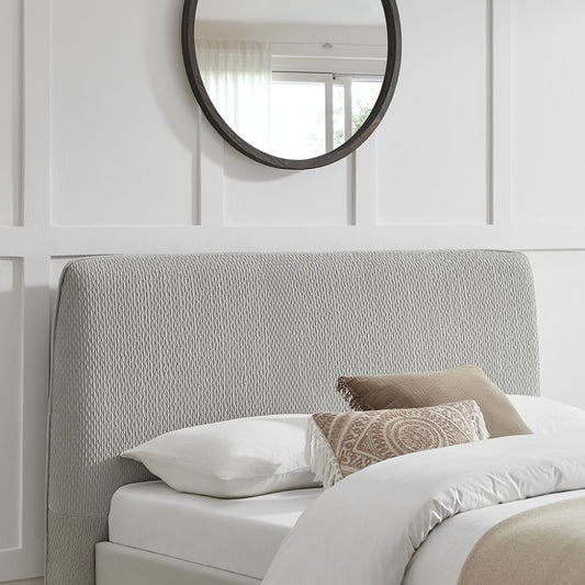 Bedroom with a textured headboard and round mirror on the wall.