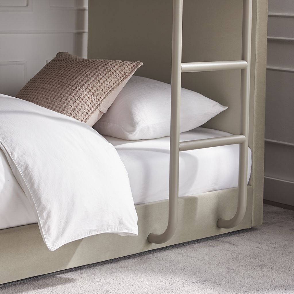 Beige bed with white bedding and a pillow, next to a ladder against a wall.