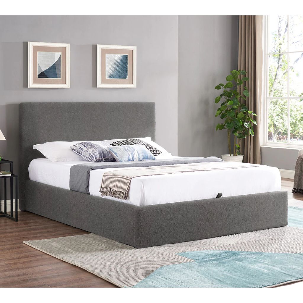 Grey upholstered bed in a bedroom with gray walls, a rug, and a plant.