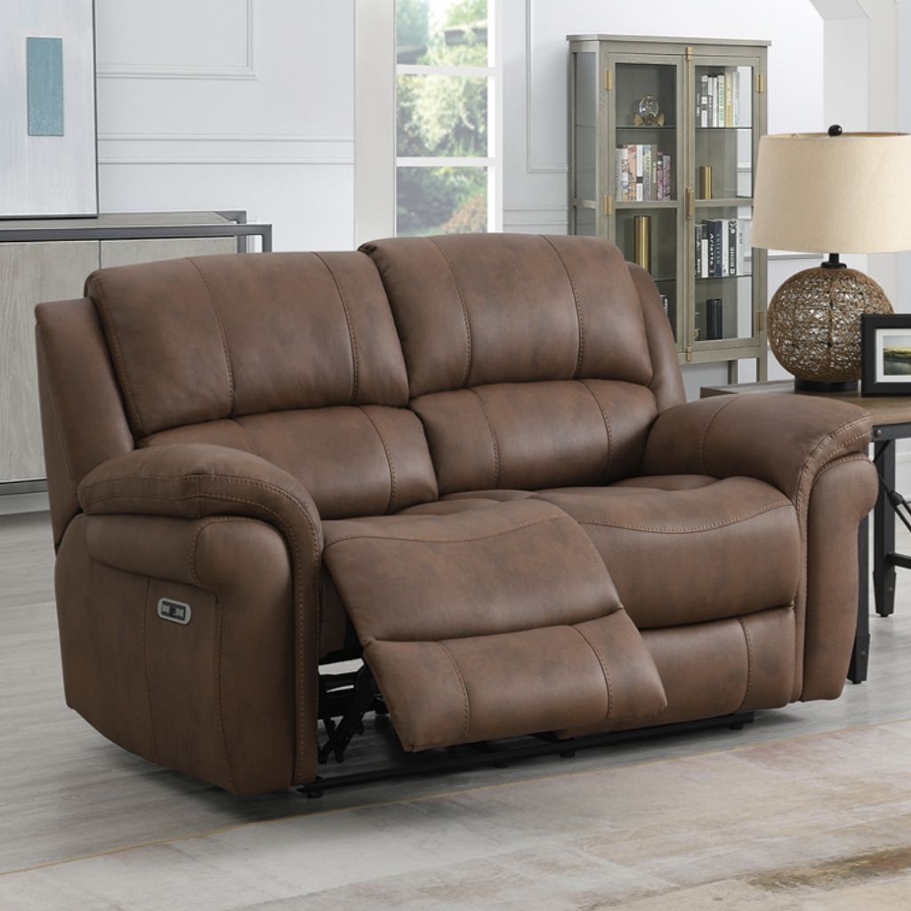 Brown fabric reclining sofa in a living room setting with a lamp and bookshelf.