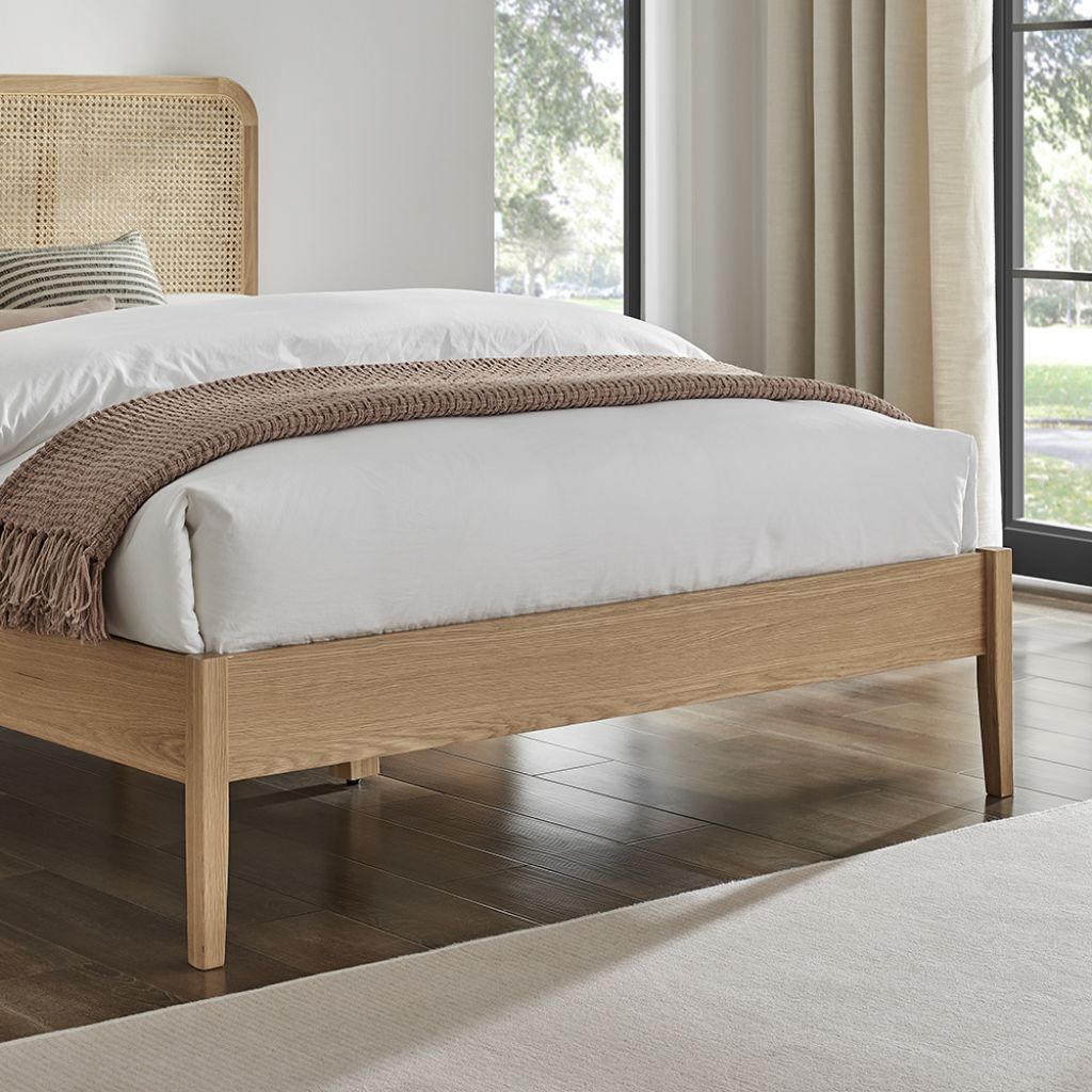 Wooden bed with white bedding and a brown throw blanket in a bright room.