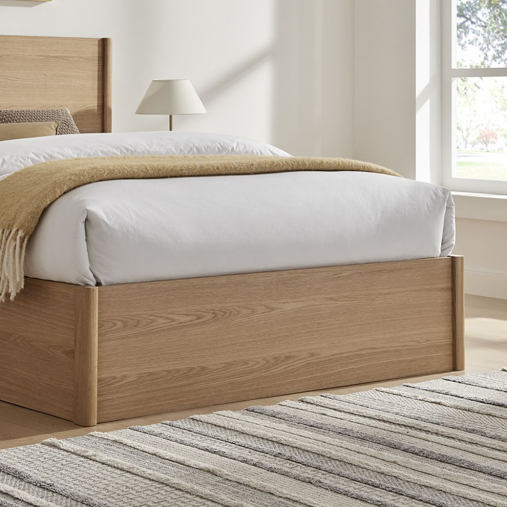 Wooden bed with white bedding and a beige blanket in a bright bedroom.