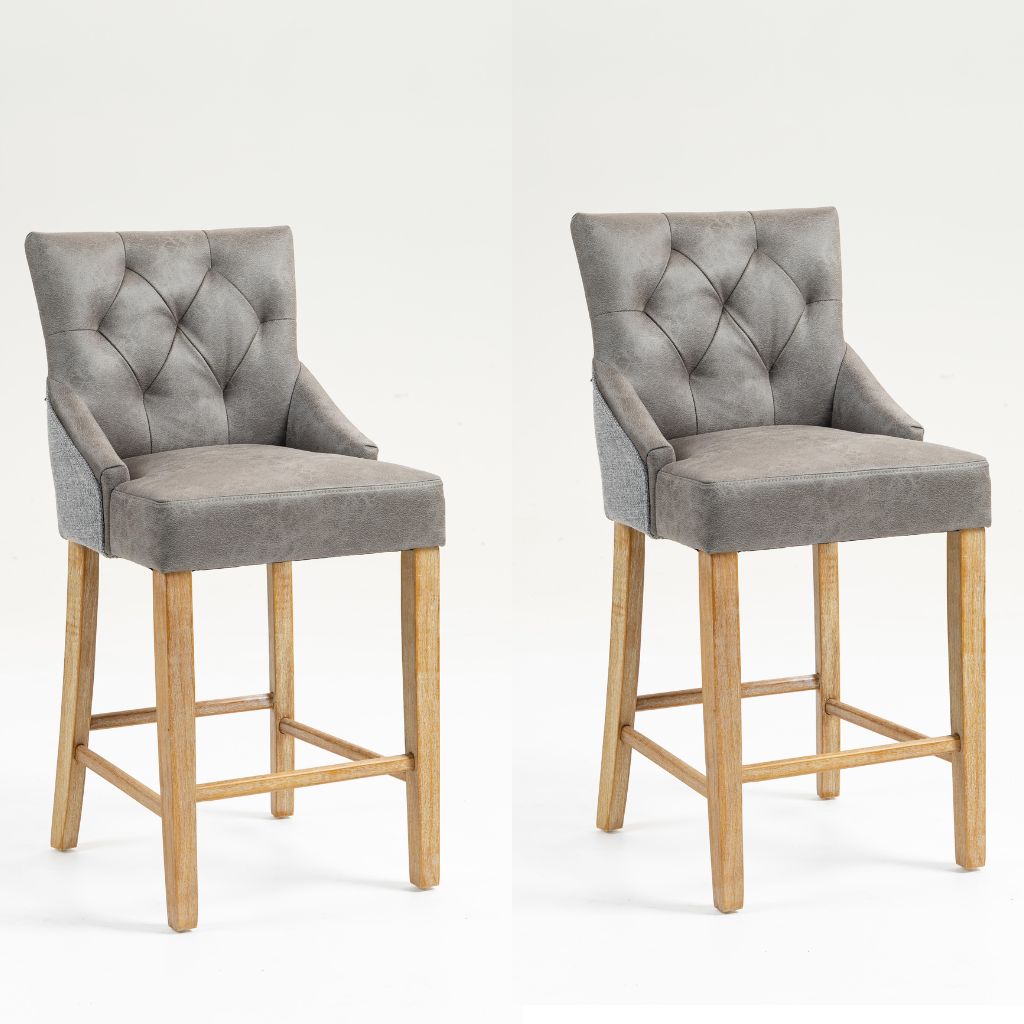 Two matching bar stools with grey tufted faux leather upholstery and natural wood legs.