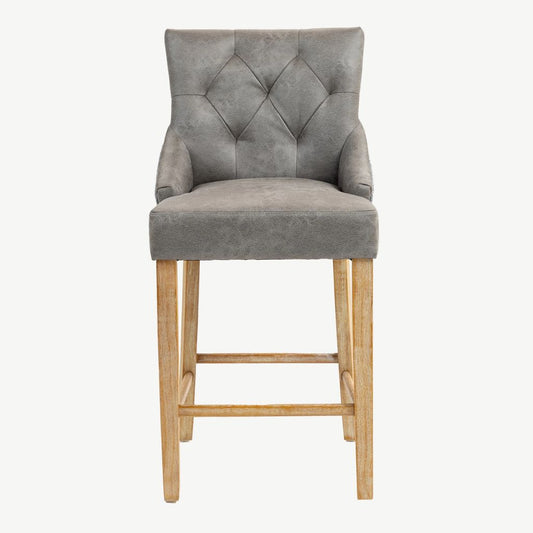 A grey PU upholstered bar stool with a diamond-tufted backrest, armrests, and natural wood legs and footrest.