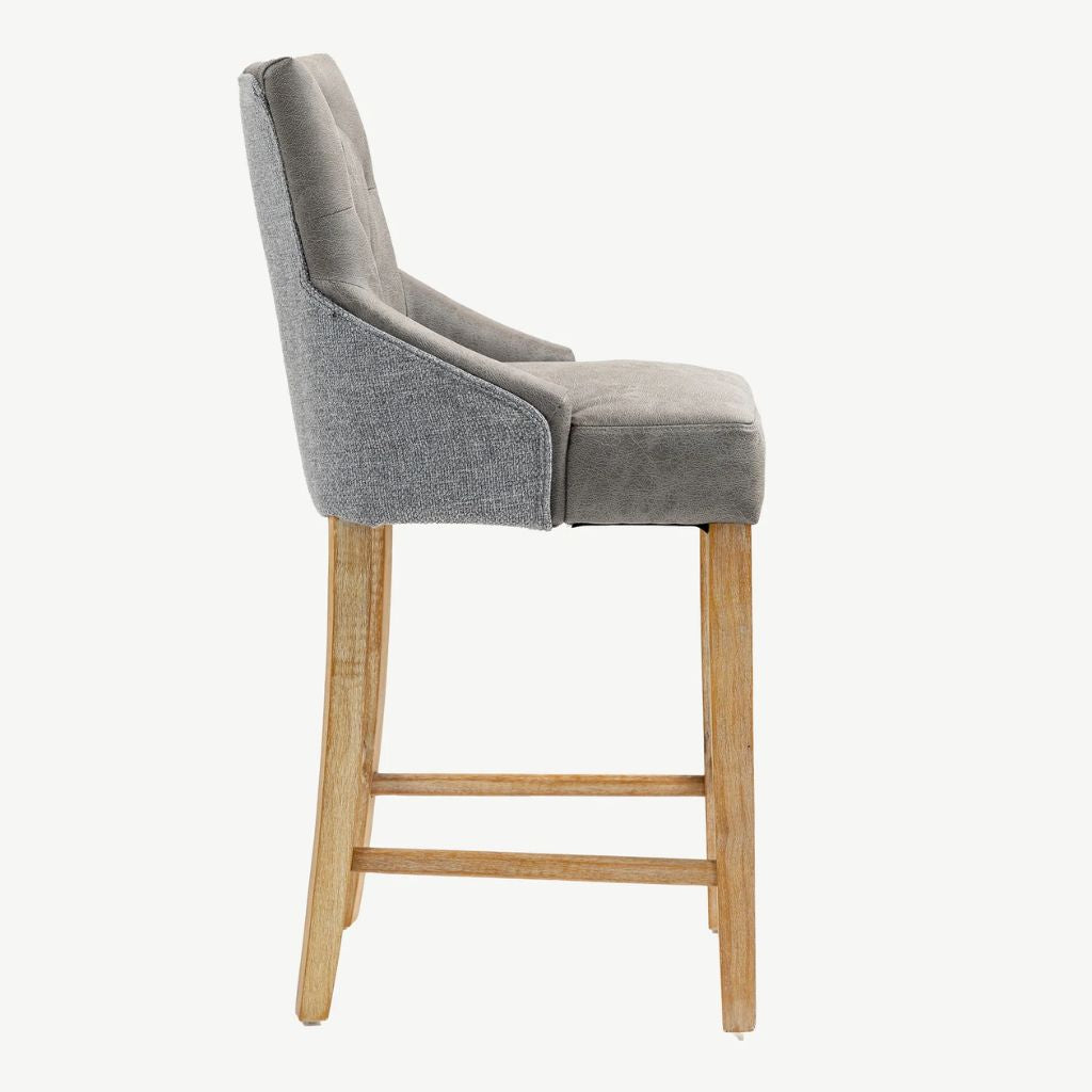 A modern bar stool with a grey upholstered seat and backrest, supported by four light natural wood legs with a central footrest, shown from a side profile view.