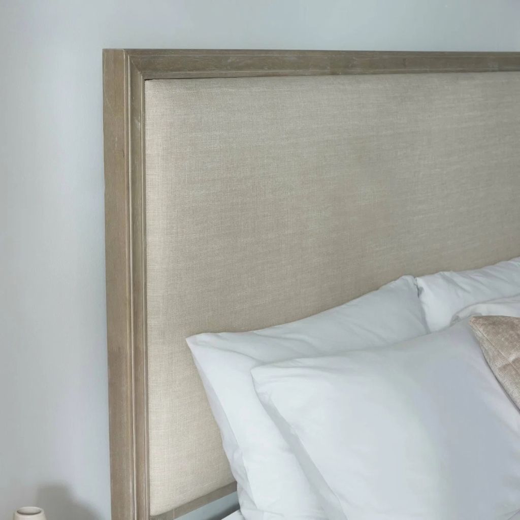 A close-up of a bed headboard upholstered in textured ivory fabric with a light wood frame.