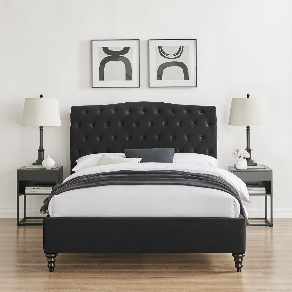 Black upholstered bed with white bedding in a room with two lamps and wall art.