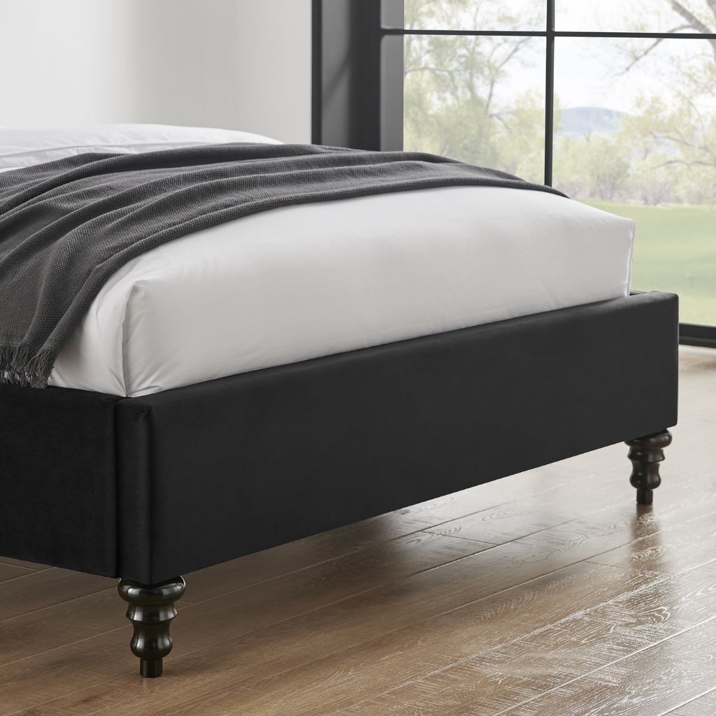 Black bed frame with white mattress and gray blanket in a room with large windows.