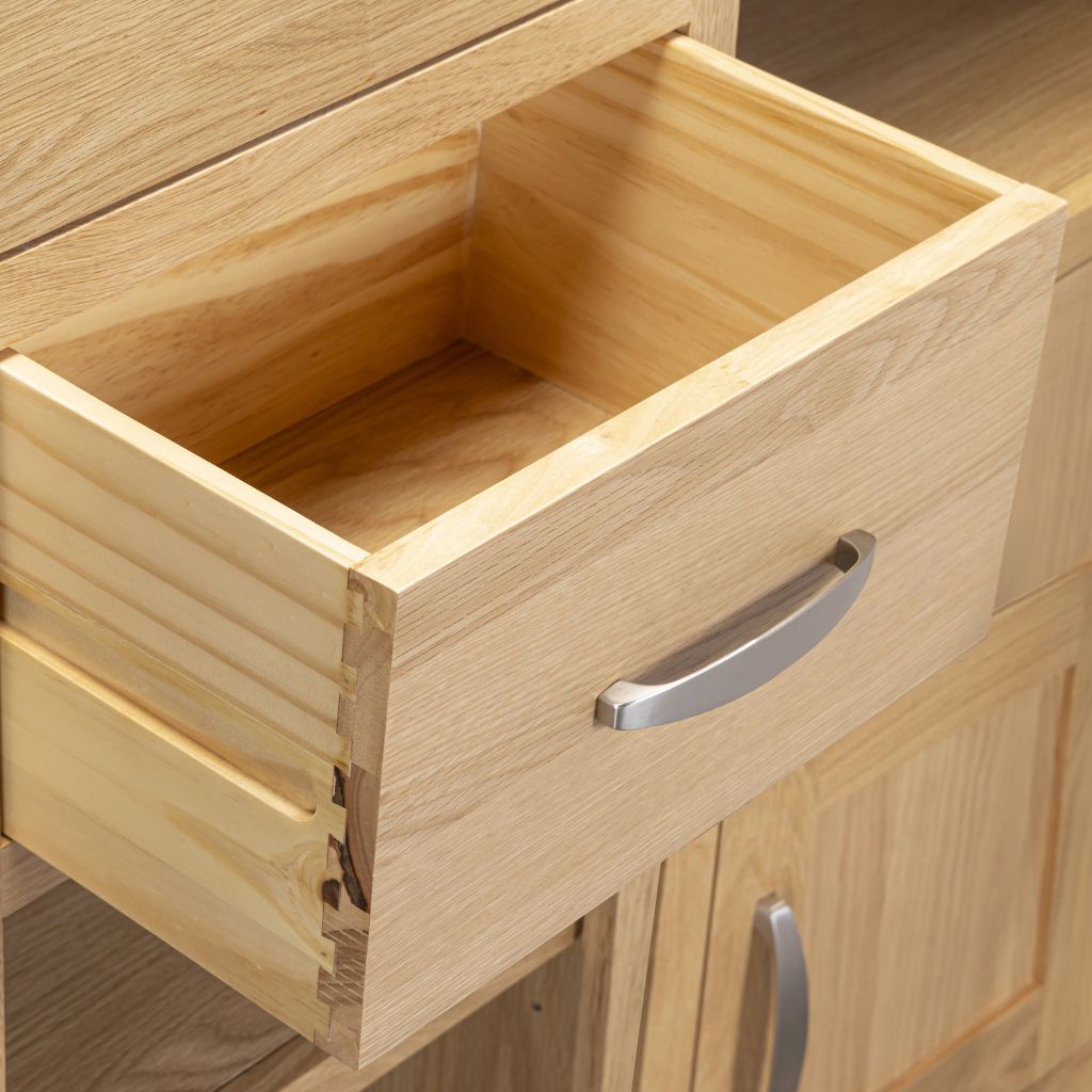 A close-up of wood drawer pulled open, showing a silver metal handle and dovetail joints.