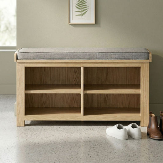 A light natural wood bench with a grey upholstered cushion on top and four open storage shelves underneath for storing shoes.