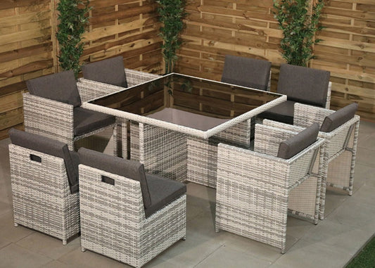 Outdoor patio dining set with glass-top table and eight cushioned rattan chairs.